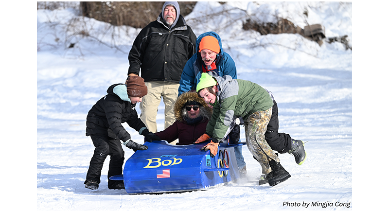 three kids and two adults with a cardboard sled entry at Beacon Field for Winter Carnival